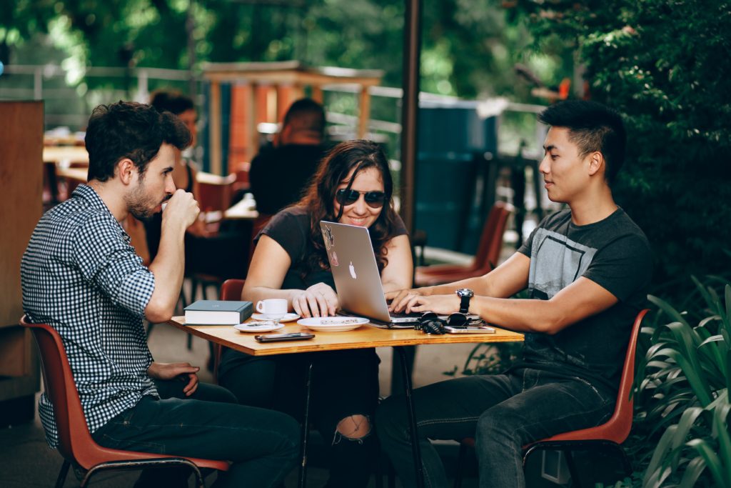 Group of 3 meeting at a coffee shop, looking at a laptop